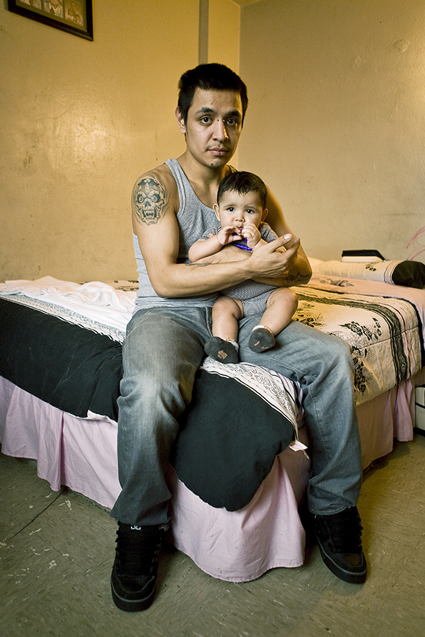 A tattooed and pierced man sits with his baby on his lap in a protective embrace