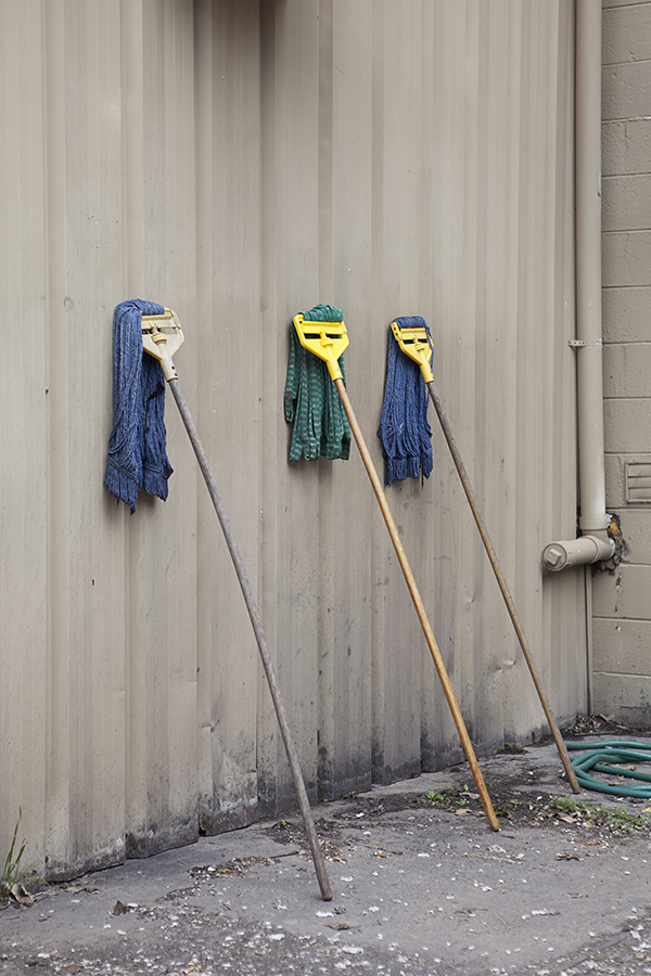 Three mops stand against a wall drying out behind a restaurant resembling people