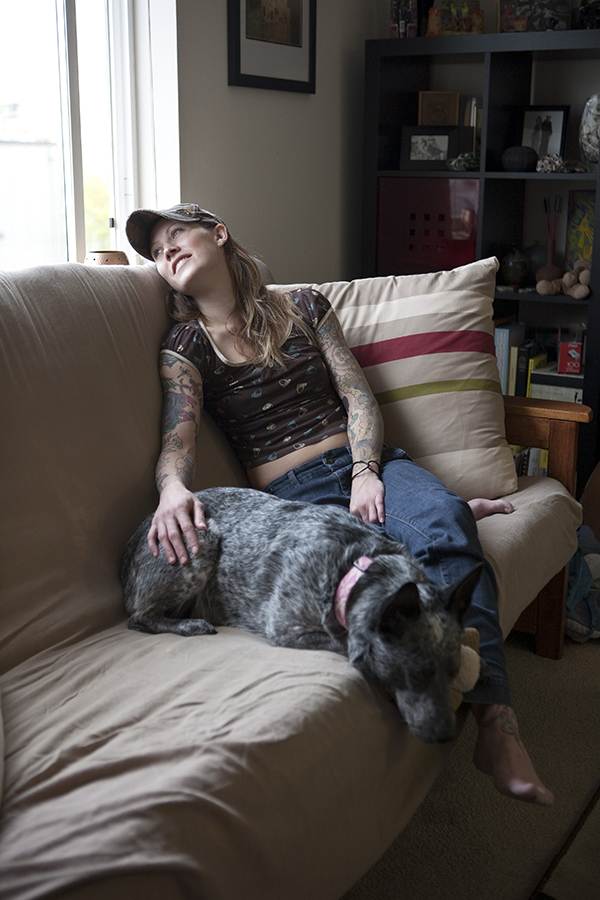 A woman sits on a couch with her dog by her side gazing out her living room chair