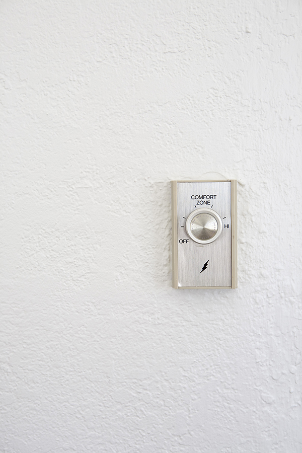 An outdated thermostat sits on a white wall with the ability to dial into the Comfort Zone