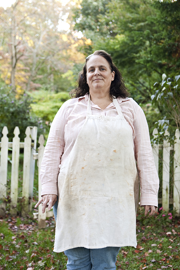 A portrait of a mother in her front yard wearing a stained apron and a smile on her face