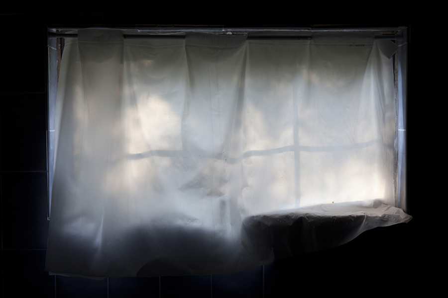 The setting sun sends light through a plastic curtain in the window of a bathroom creating a silhouette